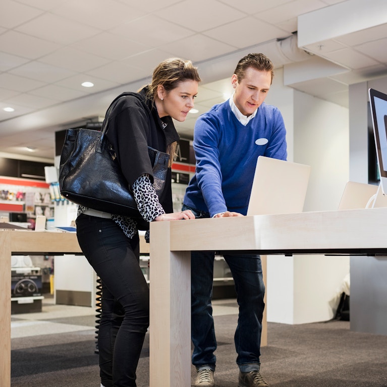 Salesman assisting female customer in buying laptop at store