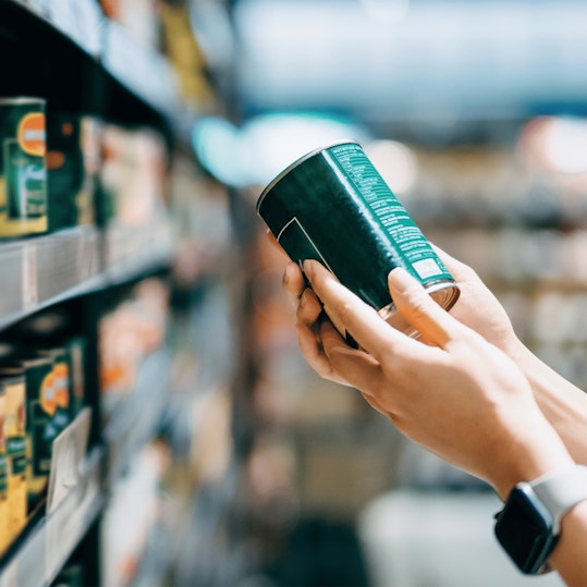 Close up of a woman grocery shopping in supermarket. Holding a tin can and reading the nutrition label at the back