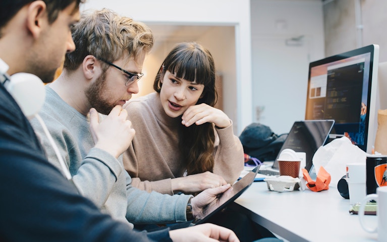 Male and female computer programmers discussing over digital tablet at desk in office